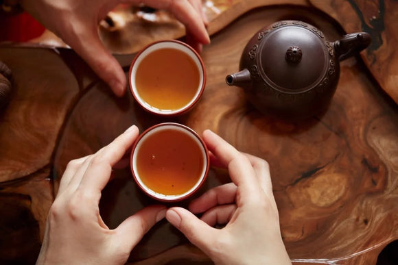 two hands holding cups of tea on a wooden table